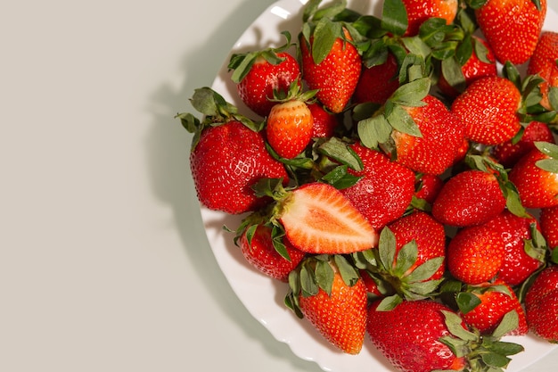 Ceramic plate with ripe red strawberry with leaves over a grey background. Space for text