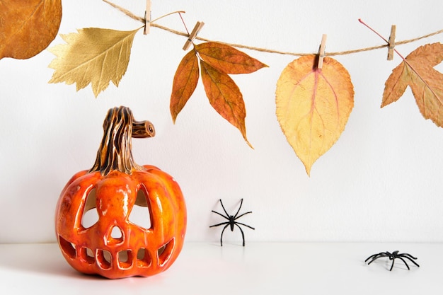 Ceramic pumpkin jack lantern and autumn leaves garland on table wall background Home decoration