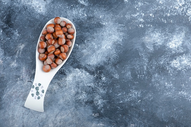 Ceramic spoon of shelled organic hazelnuts on marble.