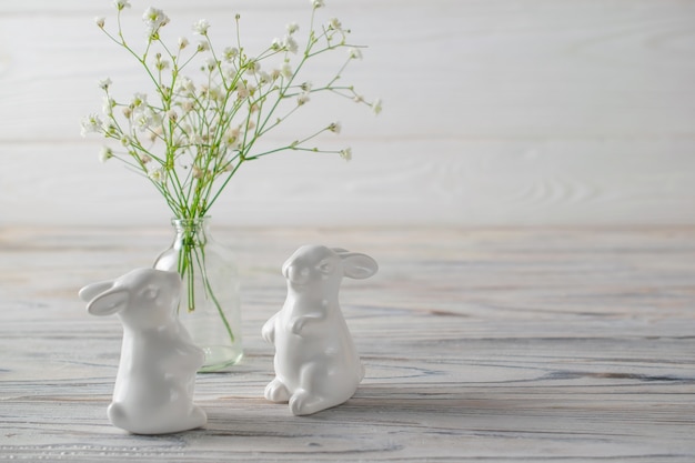 Ceramic white bunnies on white wooden table with fresh white spring flowers