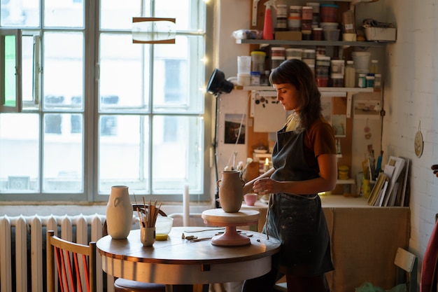 Ceramist girl in studio young self employed woman in apron creating pottery for kitchenware shop