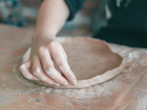 Ceramist hands make a plate of clay