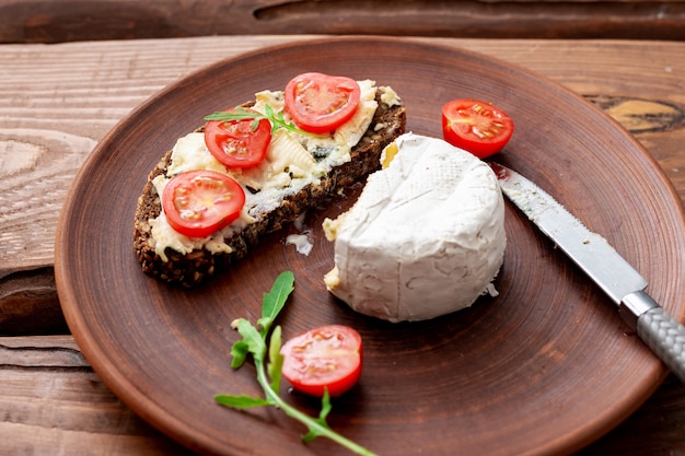 Cereal bread with blue cheese and cherry tomatoes on a clay plate on a wooden background. Healthy vegetarian food.