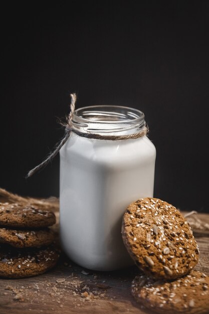 Cereal cookies with a jug of milk on a wooden background.