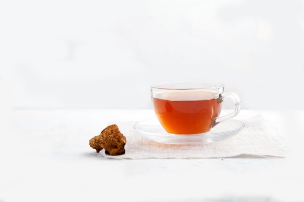 Chaga tea in a glass cup and pieces of chaga on a light background