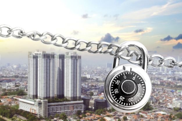 Chain of metal steel with padlock and cityscape with a blue sky background