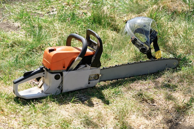 Chainsaw and protective face shield, helmet on the green grass on a sunny day. Concept is to cut trees