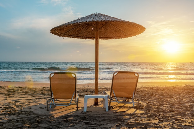 Chairs under beach umbrella on tropical beach during sunset