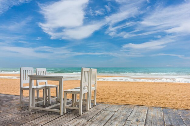 Photo chairs and table on boardwalk at beach against sky