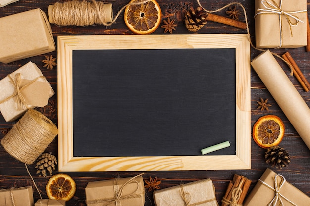 Chalk board in the middle of gifts of dried orange, cinnamon, pine cones, anise