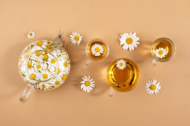 Chamomile tea Cups of herbal tea transparent teapot with camomile flowers on brown background Calming drink concept Trendy still life