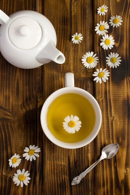 Chamomile tea in the white cup and teapot on the wooden background. Top view. Close-up.