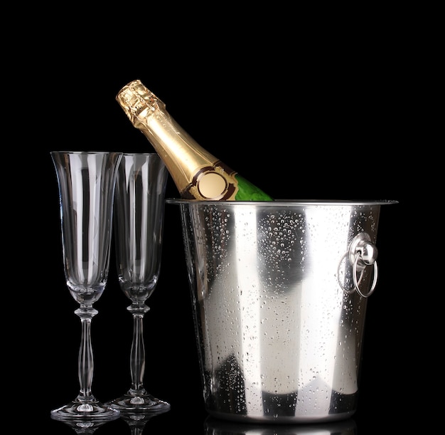 Champagne bottle in bucket with ice and glasses isolated on black