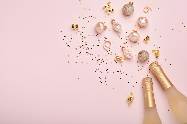 Champagne bottle, gift or present box and golden shiny sparkle star confetti on pink background. Christmas or New Year composition or card. Celebration flat lay. Party creative concept. Top view.