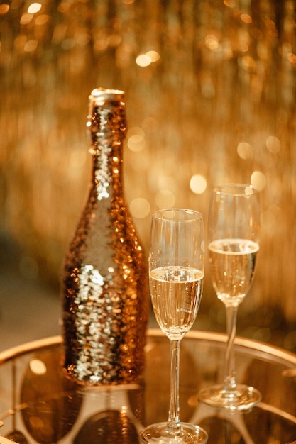 Champagne bottle and glasses against luxury glow golden rain decoration expensive holidays party