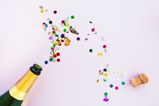 Champagne bottle with bright confetti on a pink background