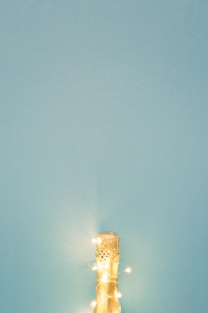 Champagne bottle with garlands on color background top view