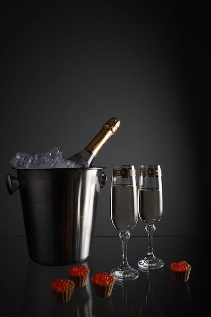 Champagne glasses with ice and a bucket for cooling the bottle against a dark wall