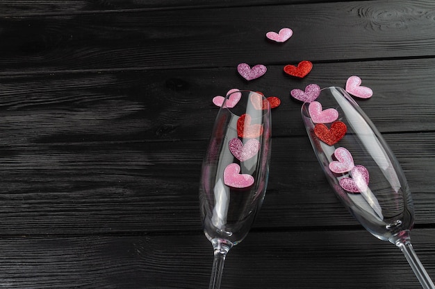 Champagne glasses with sequin hearts on black desk top view flat lay