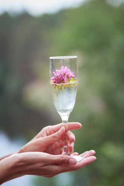 Champagne with wildflowers outsideWomen39s hands keeps a glass with champagne with surreal flowers Celebrating life and solitude concept Vertical photo High quality photo