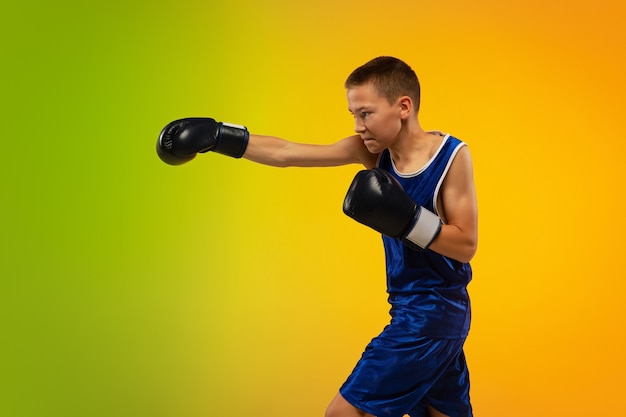 Champion. Teenage professional boxer training in action, motion isolated on gradient background in neon light. Kicking, boxing. Concept of sport, movement, energy and dynamic, healthy lifestyle.