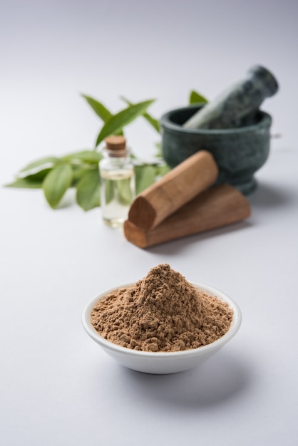 Chandan or sandalwood powder with sticks, traditional mortar, perfume or oil in miniature bottle and green leaves. selective focus