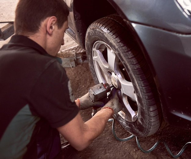 Changing car wheel and tyre in auto repair service Focus on professional mechanic hands with pneumatic wrench in action