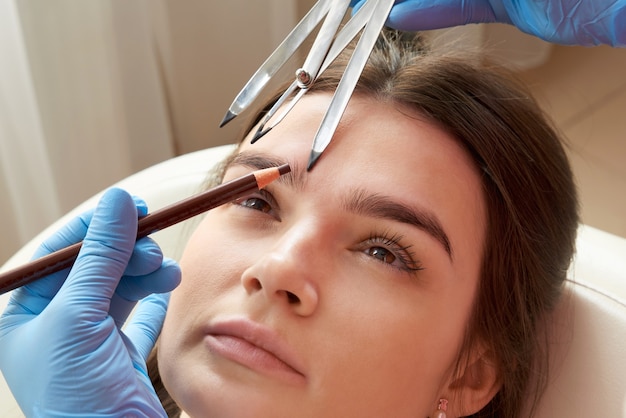 Changing the shape of the brows. Stylist measuring the eyebrows with the ruler. Micropigmentation work flow in a beauty salon. Woman having her eye brows tinted with Semi-permanent makeup.