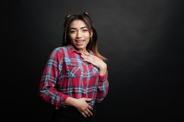 Charismatic playful Latino American woman expressing femininity and smiling while standing in the black colored studio