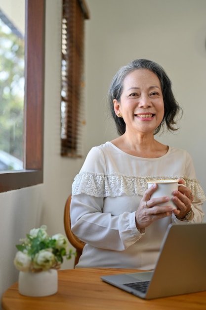 Charming 60s retired Asian woman holding a tea cup smiling and looking at the camera