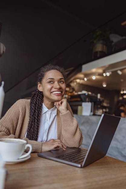 Charming african girl smiles cutely looking away sitting in cafe with a cup of coffee