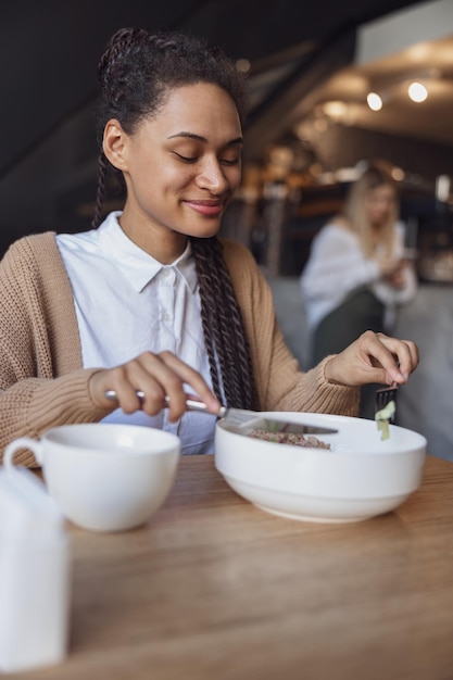 Charming african young woman in casual clothes enjoying her lunch during lunch break at food