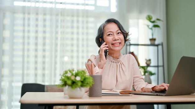 Charming agedasian businesswoman enjoys talking on the phone while working in her office