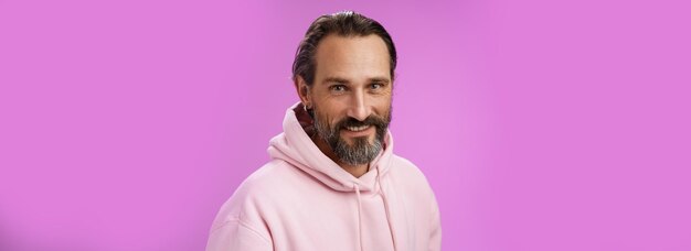 Charming alluring handsome bearded stylish adult male model earring pink hoodie smiling delighted