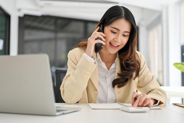 Charming Asian businesswoman calculating profit during the call with her client