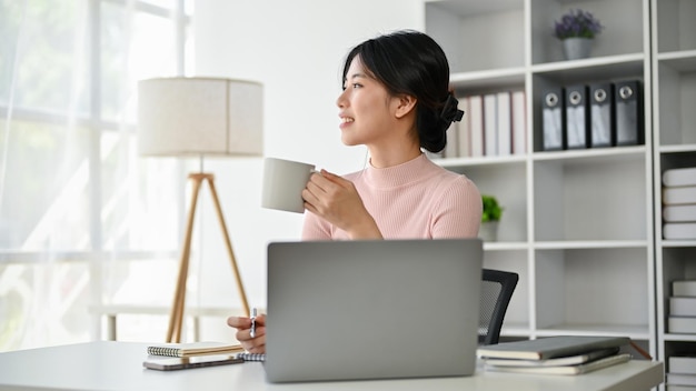 A charming Asian businesswoman enjoying her morning coffee at her desk