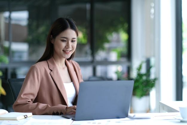 Charming asian businesswoman sitting working on laptop in office