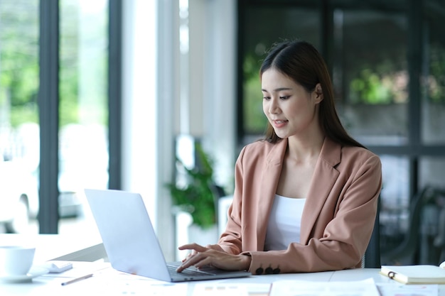 Charming asian businesswoman sitting working on laptop in office