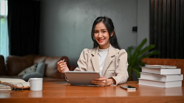 Charming Asian businesswoman using tablet at her desk smiling and looking at the camera