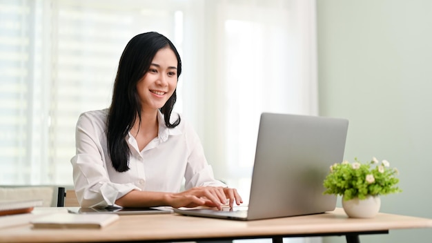 Charming Asian businesswoman working in her office typing on keyboard using laptop