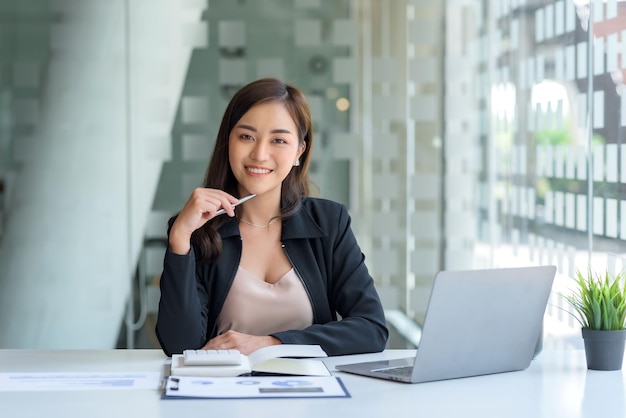 Charming Asian businesswoman working with a laptop at the office Looking at camera