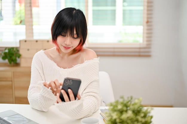 Charming Asian woman chatting with her friends using her smartphone