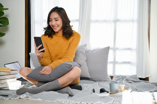 Charming Asian woman using her smartphone while relaxing in her living room