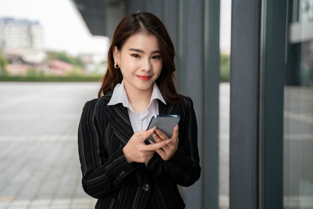 Charming Asian woman with a smile standing holding mobile phone on the street in big city portrait shot job application concept