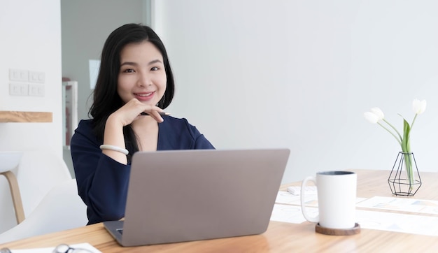 Charming Asian woman working at the office using a laptop Looking at the camera