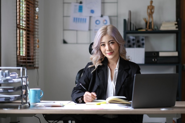 Charming Asian woman working at the office using a laptop Looking at the camera