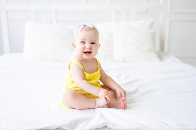 Charming baby girl in a white sunny bedroom A newborn baby is resting in bed Textiles and bedding for children Family morning at home A newborn baby is sitting on the bed after sleeping