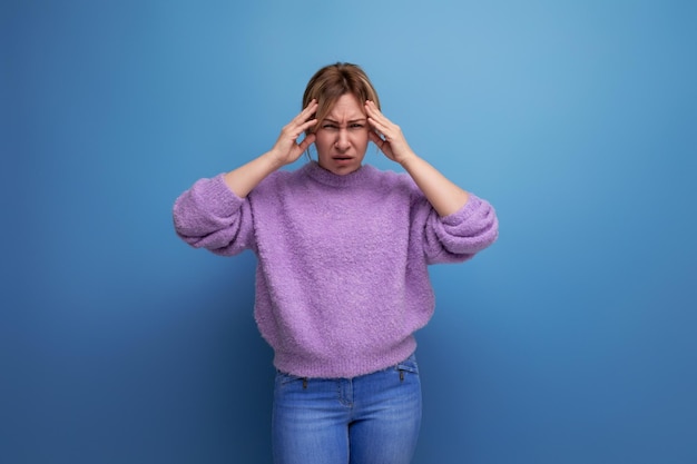 Charming blond young millennial woman in a casual look with a sore head on a bright background with