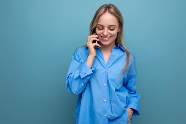 Charming blonde woman chatting in a smartphone on a blue bright background