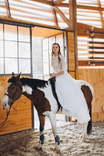 A charming boho bride rides a horse on a ranch at sunset in winter